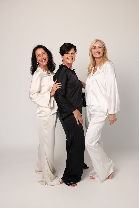 Three people in formal attire standing on a white floor with a brick wall in the corner.