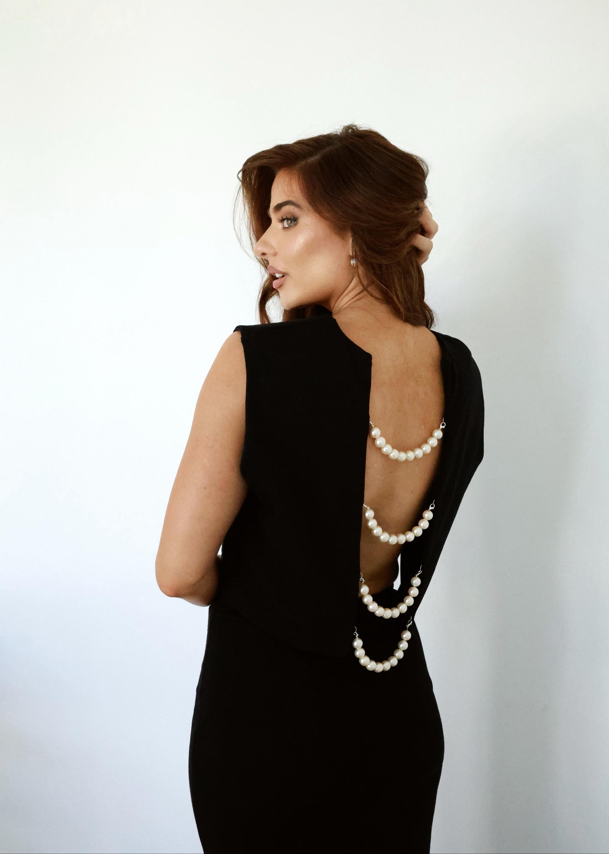 Woman wearing a black dress with a pearl necklace and bracelet against a white background