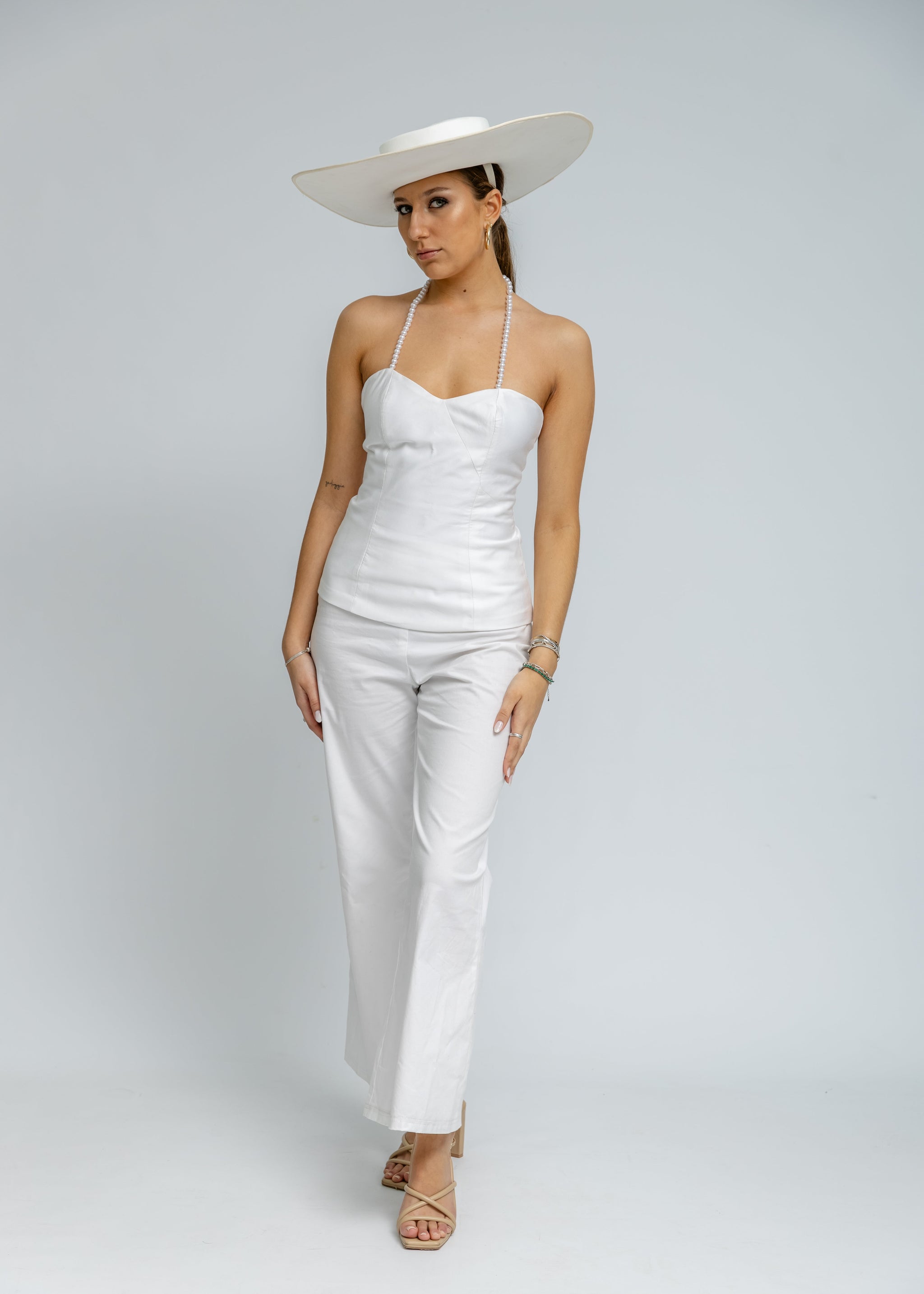 Woman wearing a white outfit with a wide-brimmed hat on a plain background