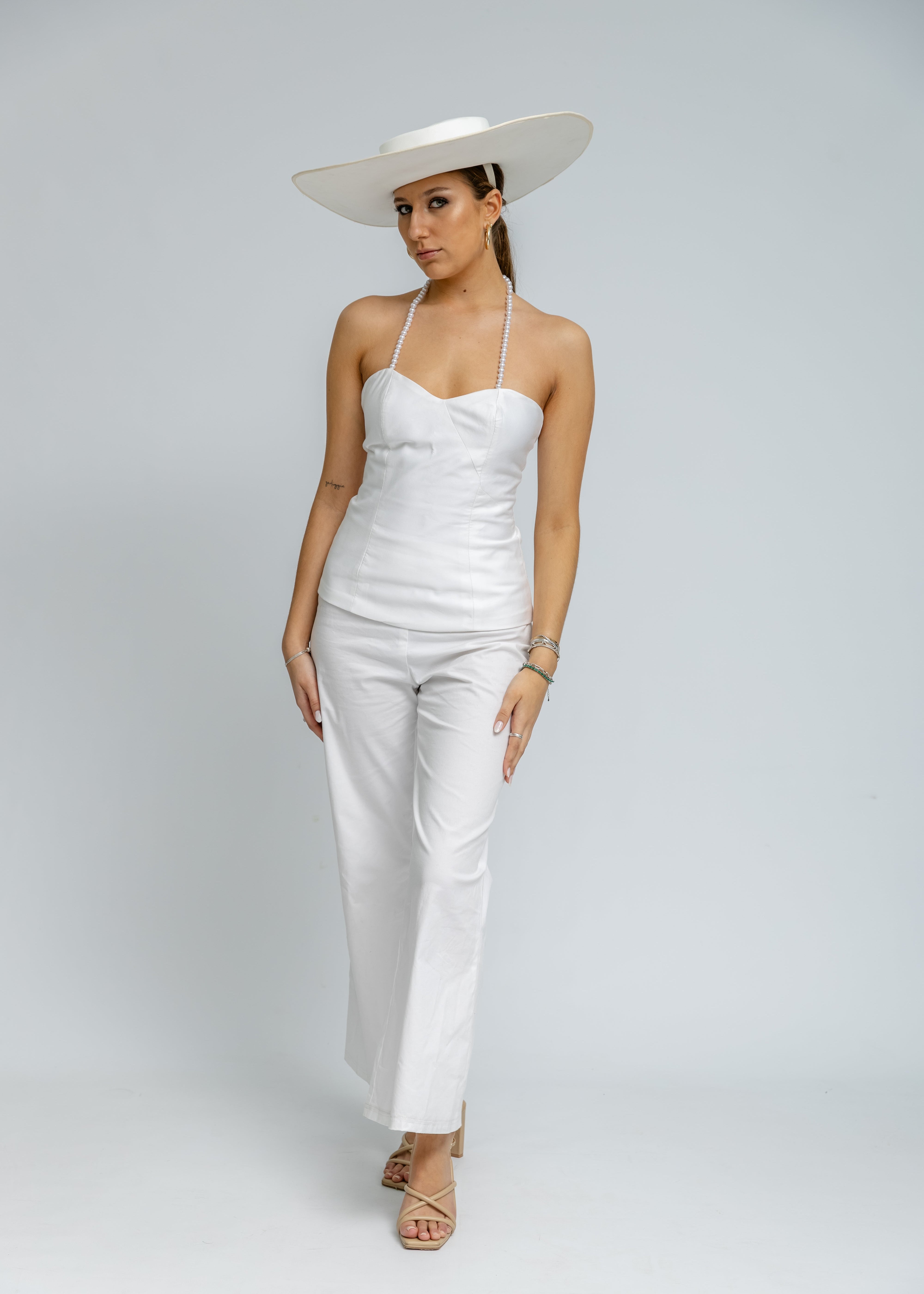 Woman wearing a white outfit with a wide-brimmed hat on a plain background
