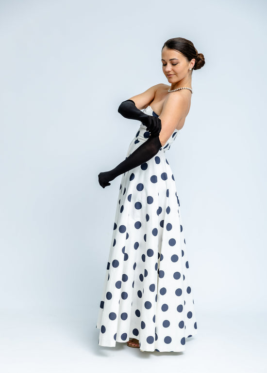 Woman wearing a white dress with blue polka dots and black gloves on a white background