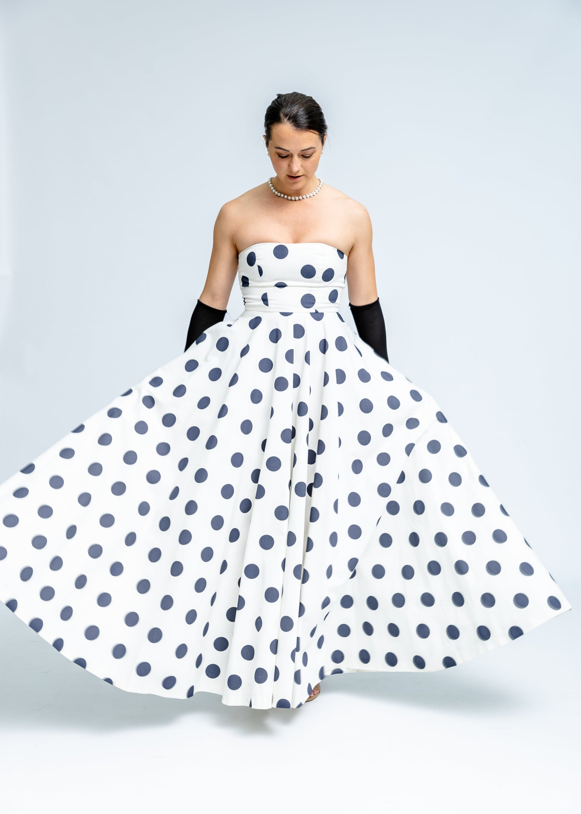 Woman wearing a strapless polka dot dress on a plain background