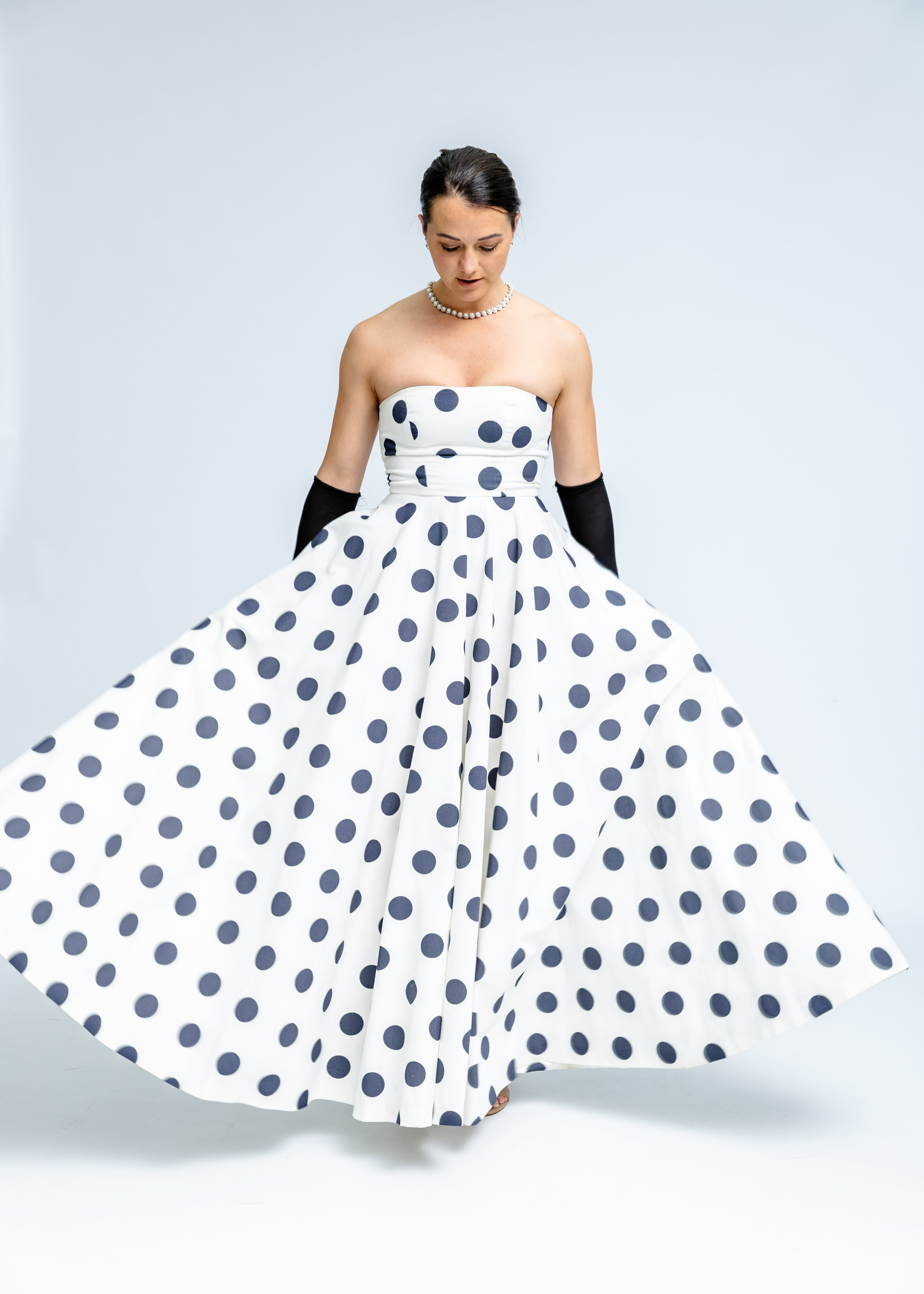 Woman wearing a strapless polka dot dress on a plain background