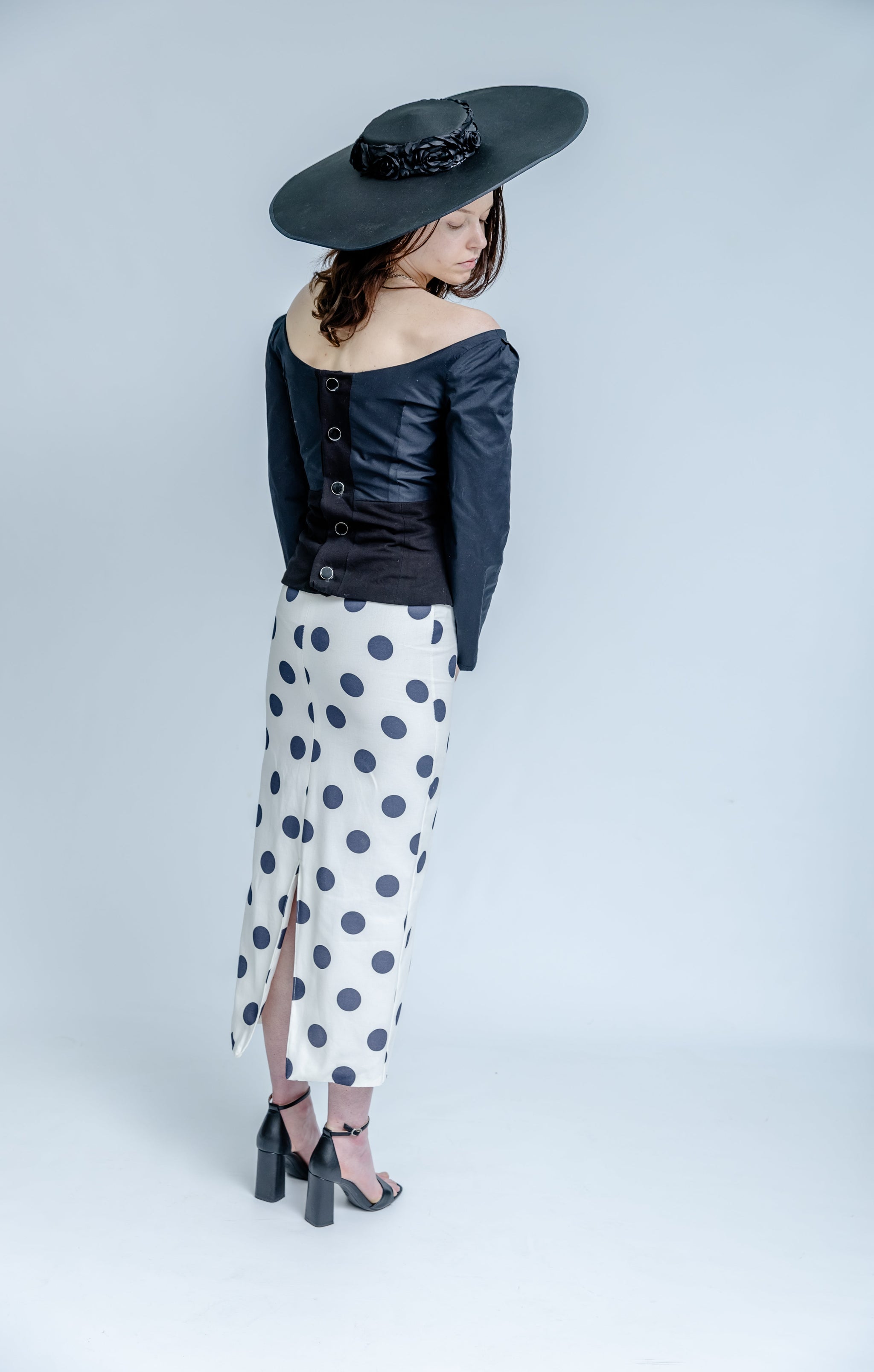 Woman wearing a black hat, dark jacket, and polka dot pants on a white background