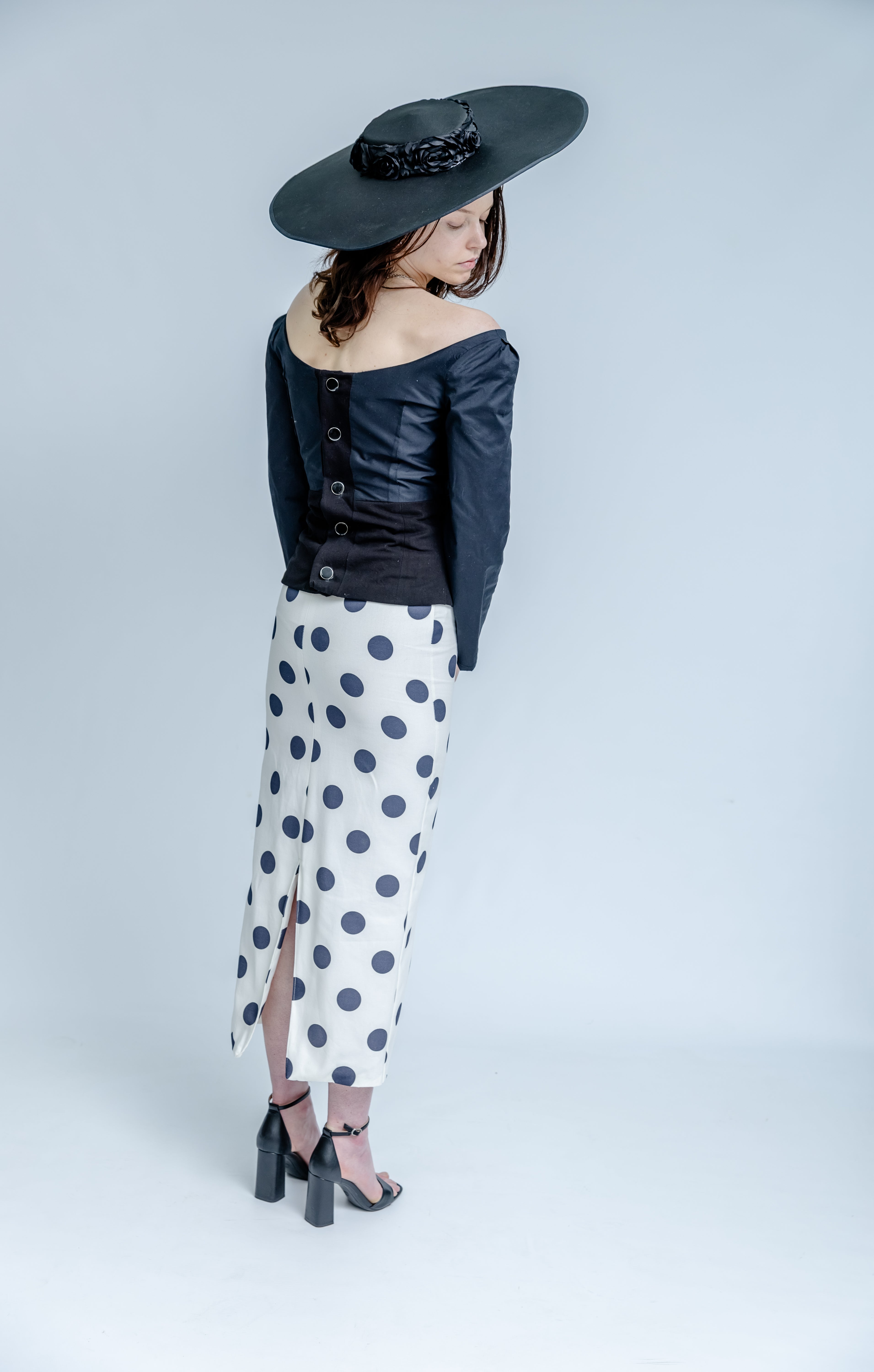 Woman wearing a black hat, dark jacket, and polka dot pants on a white background