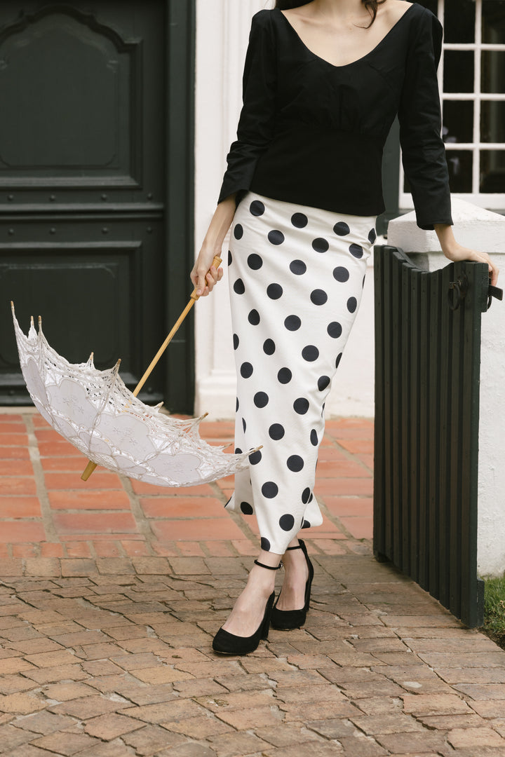 Woman in black top and polka dot pants holding a transparent umbrella on a brick path.