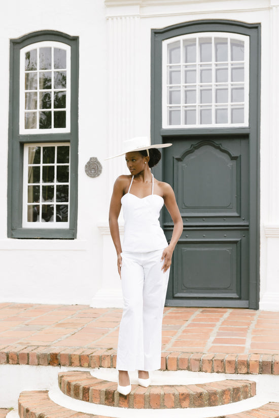 Woman in a white outfit standing in front of a white building with green shutters.