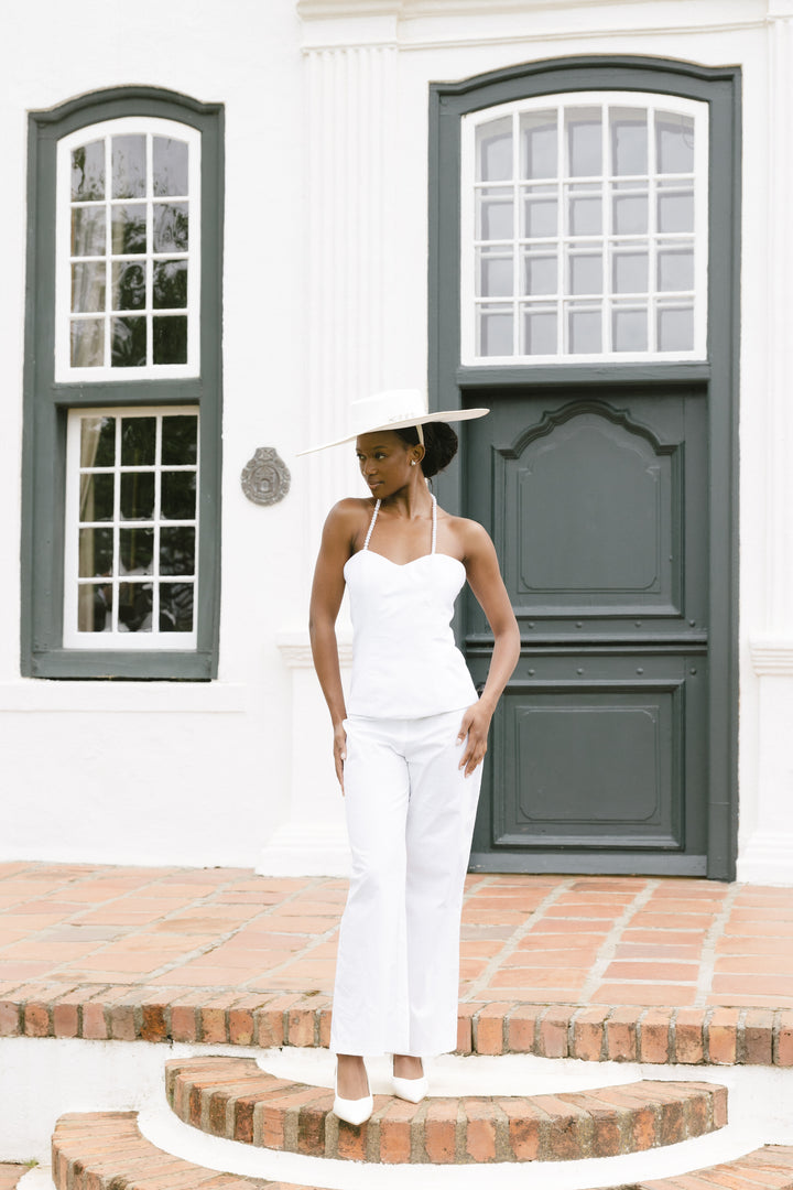 Woman in a white outfit standing in front of a white building with green shutters.