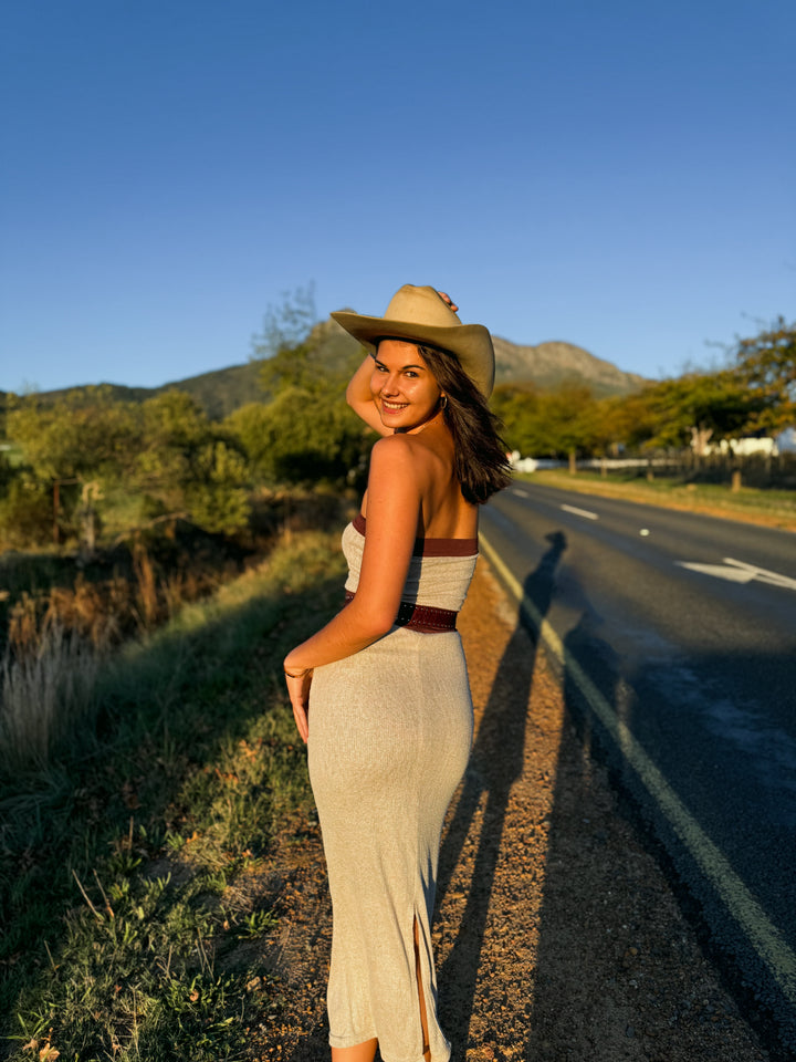 Woman in a dress and hat standing by a road with mountains in the background