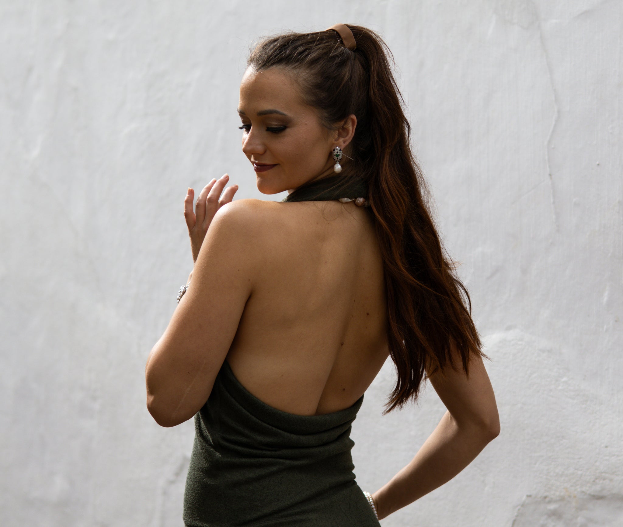 Woman in a green dress with an open back against a textured white wall