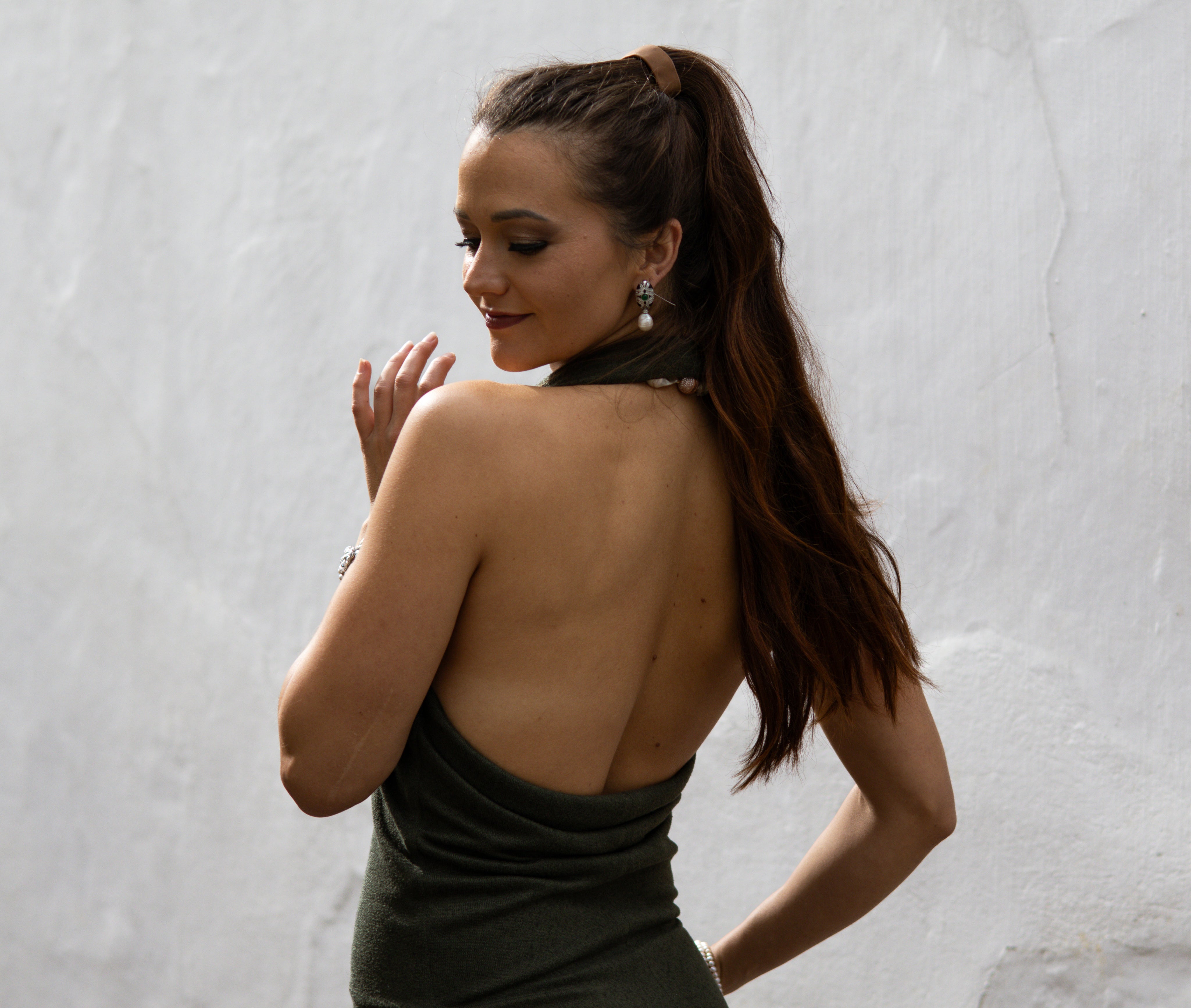 Woman in a green dress with an open back against a textured white wall