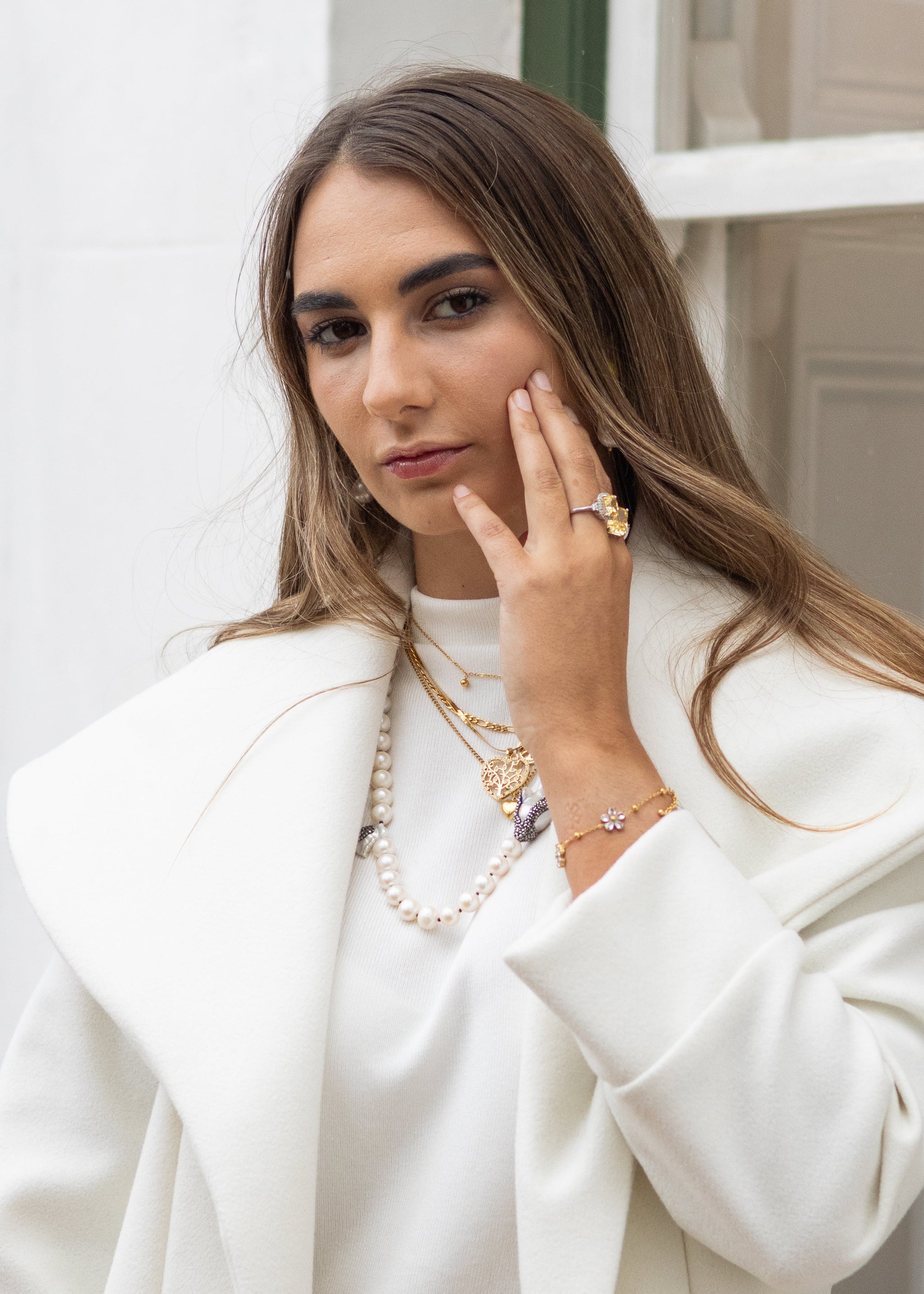 Woman wearing a white coat and gold jewelry against a neutral background