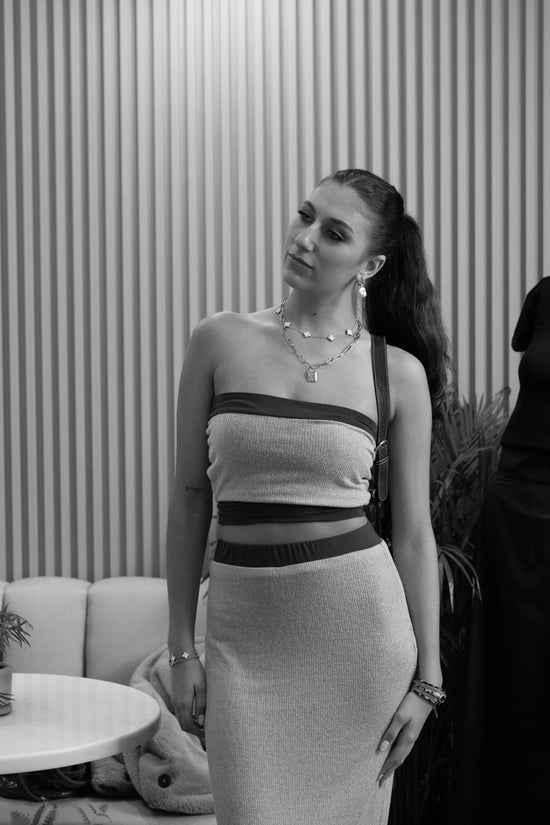 Woman in a strapless top and pencil skirt standing indoors with a striped wall background