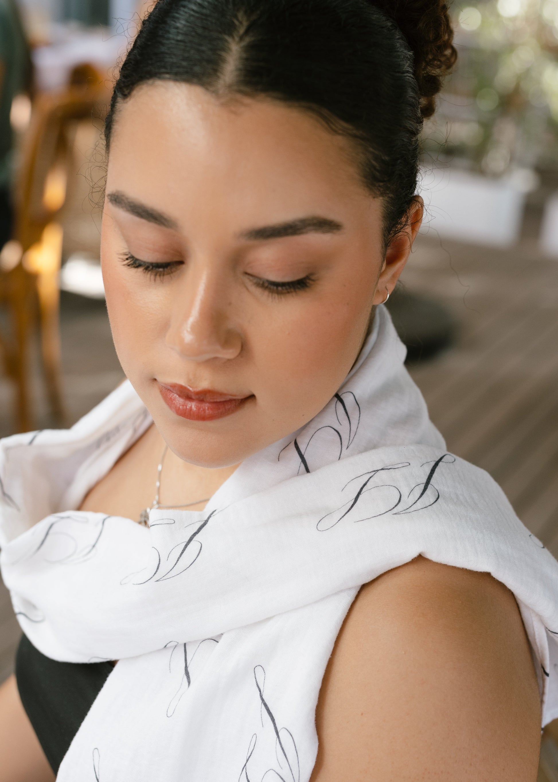 Woman wearing a white scarf with black patterns, looking down.