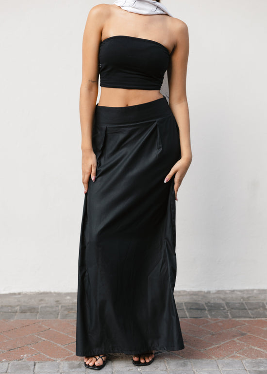 Woman wearing a black strapless top and long black skirt against a plain background