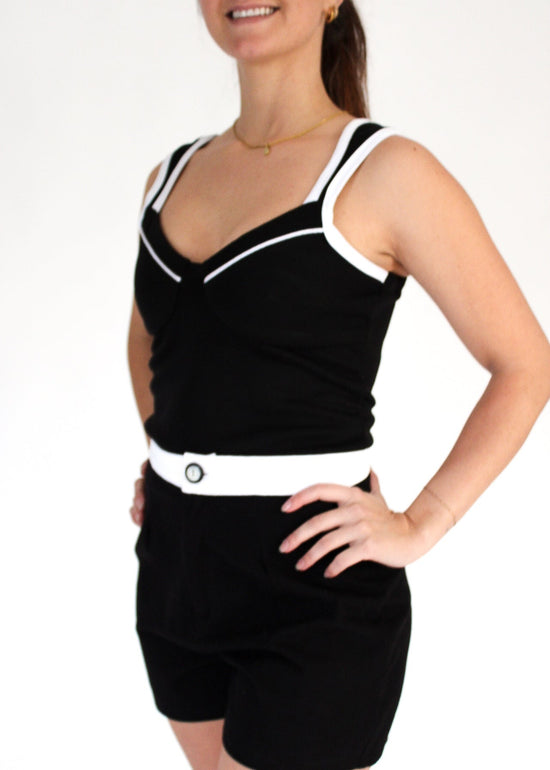 Woman wearing a black outfit with white trim on a plain background