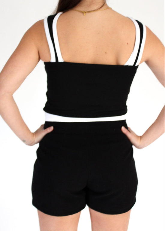 Black romper with white straps worn by a person on a white background