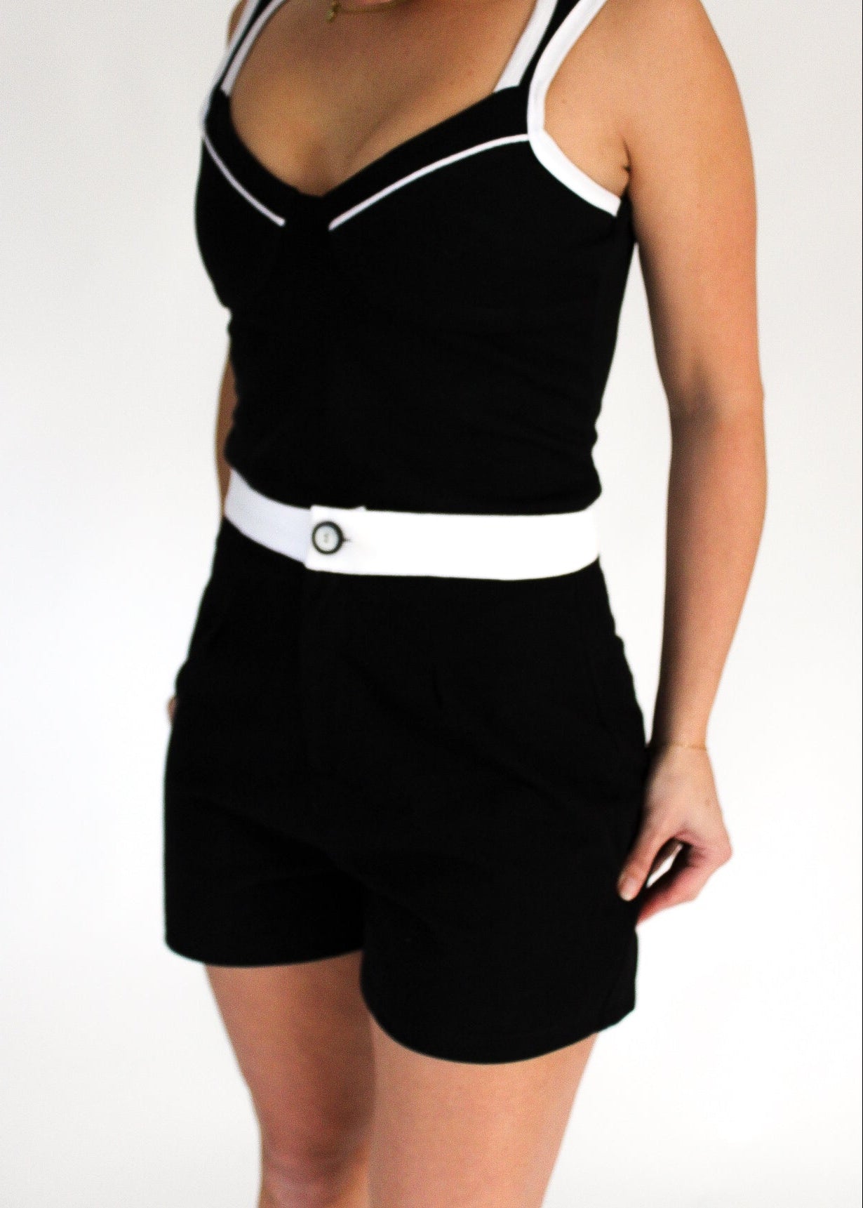 Person wearing a black tank top and shorts with a white belt on a plain background