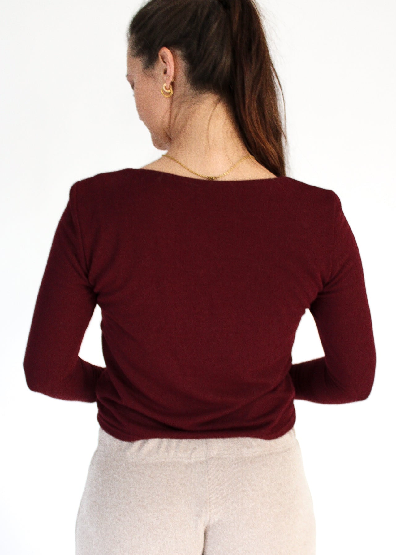Woman wearing a burgundy long-sleeve top and light-colored pants on a white background
