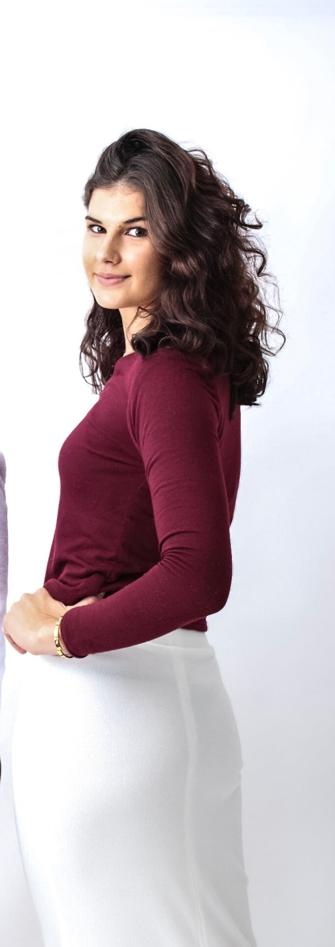 Woman wearing a burgundy long-sleeve top and white pants on a white background