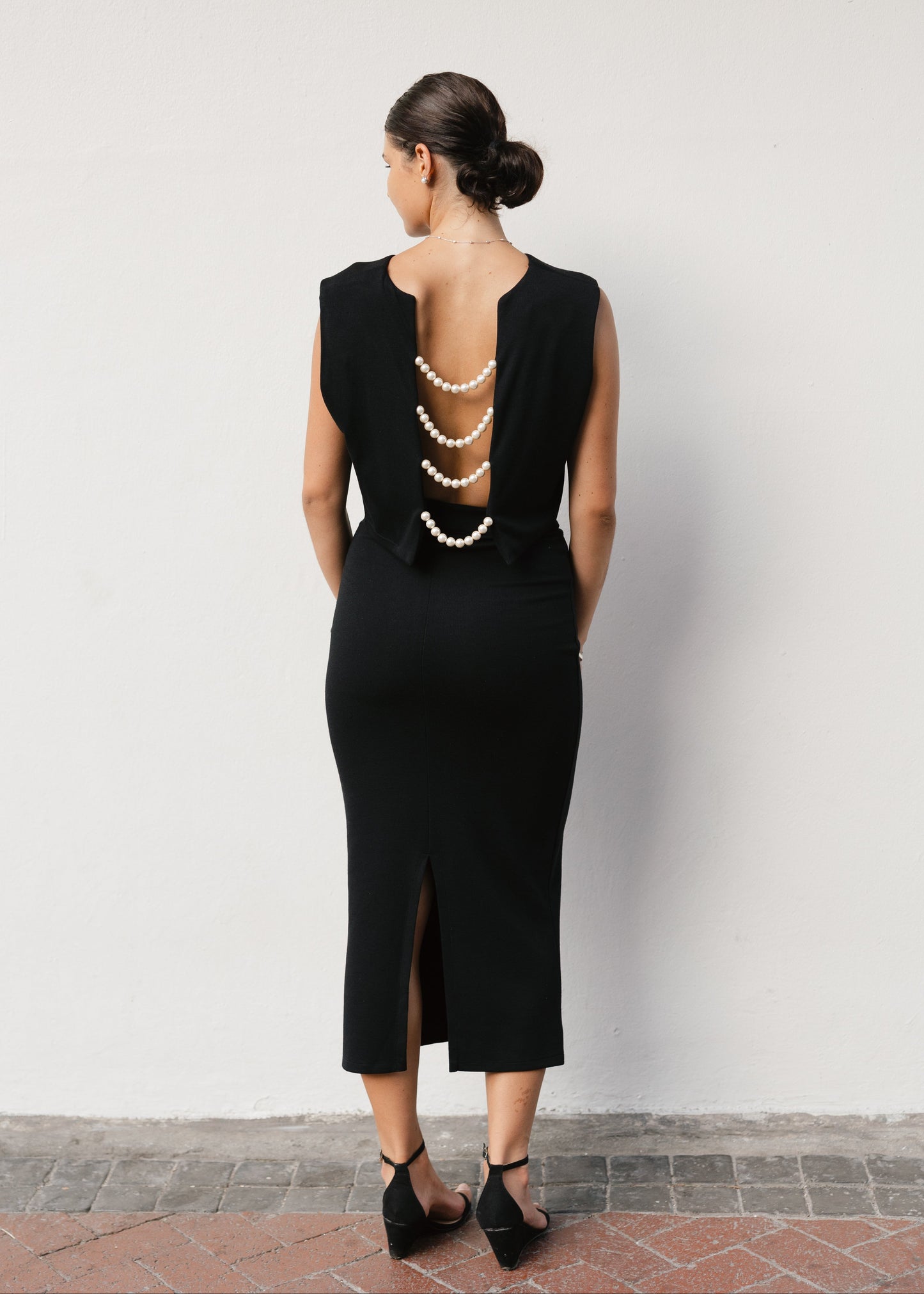 Woman wearing a black dress with a unique back design against a white wall.