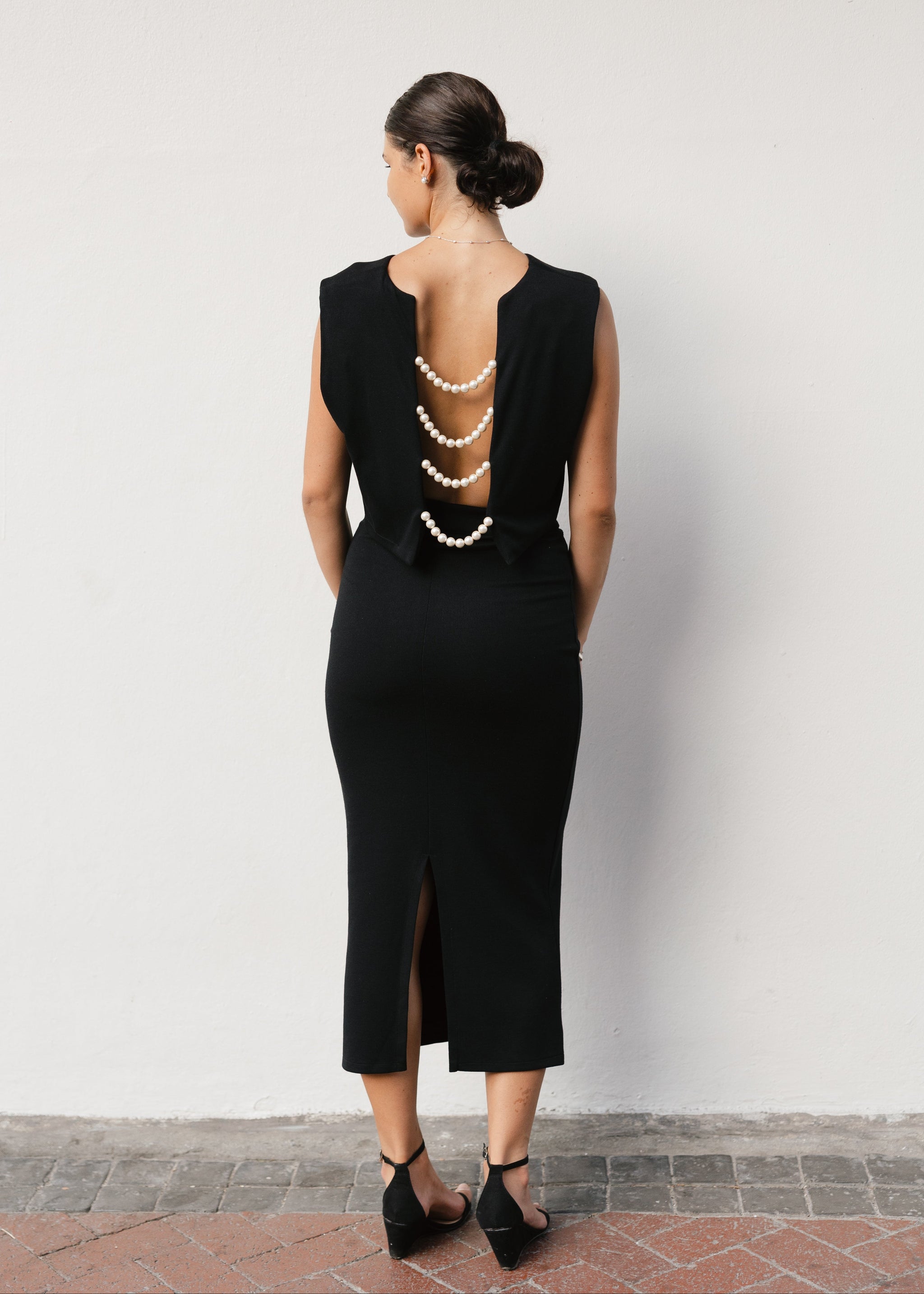 Woman wearing a black dress with a unique back design against a white wall.