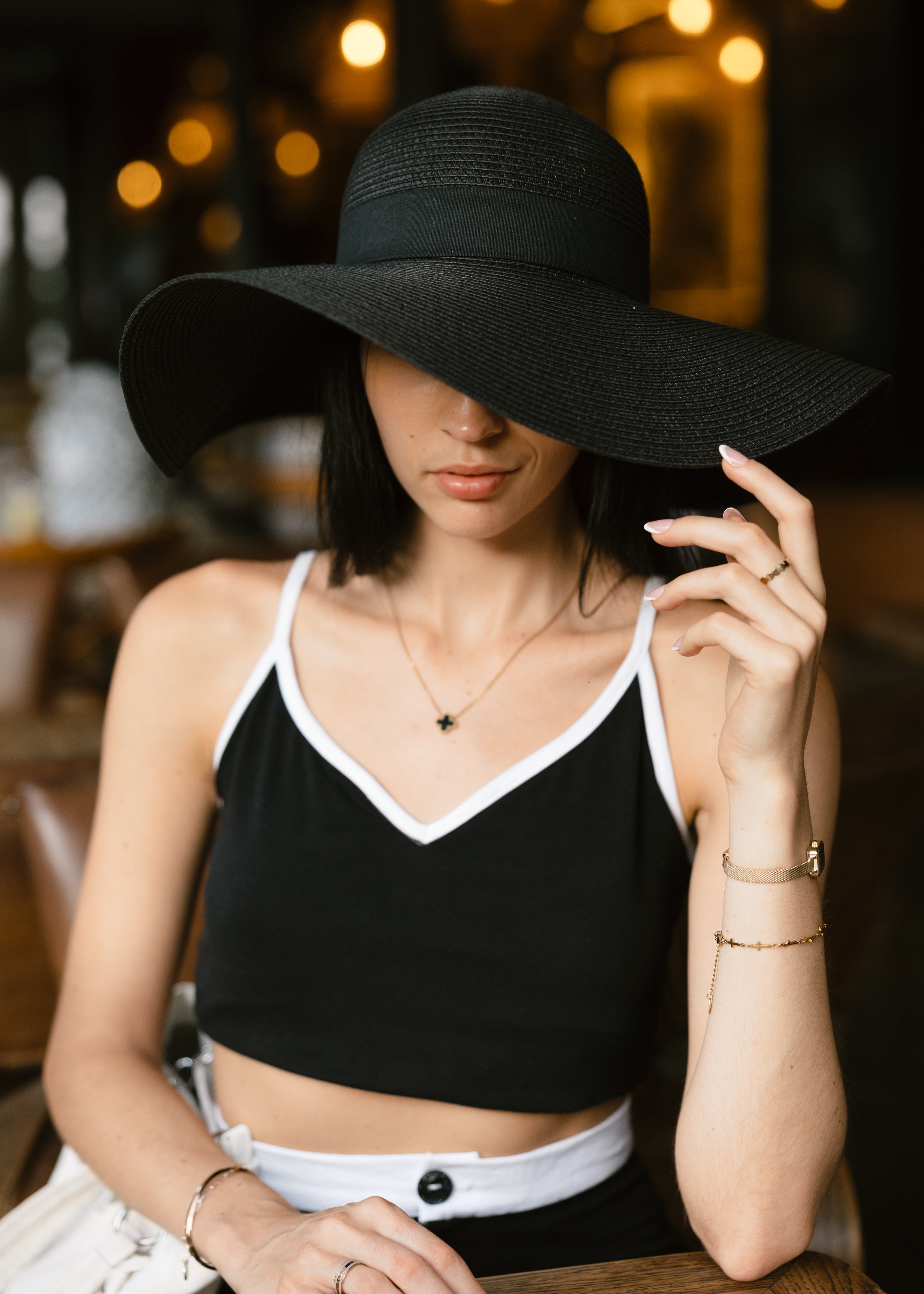 Woman wearing a black wide-brimmed hat in an indoor setting with blurred lights in the background