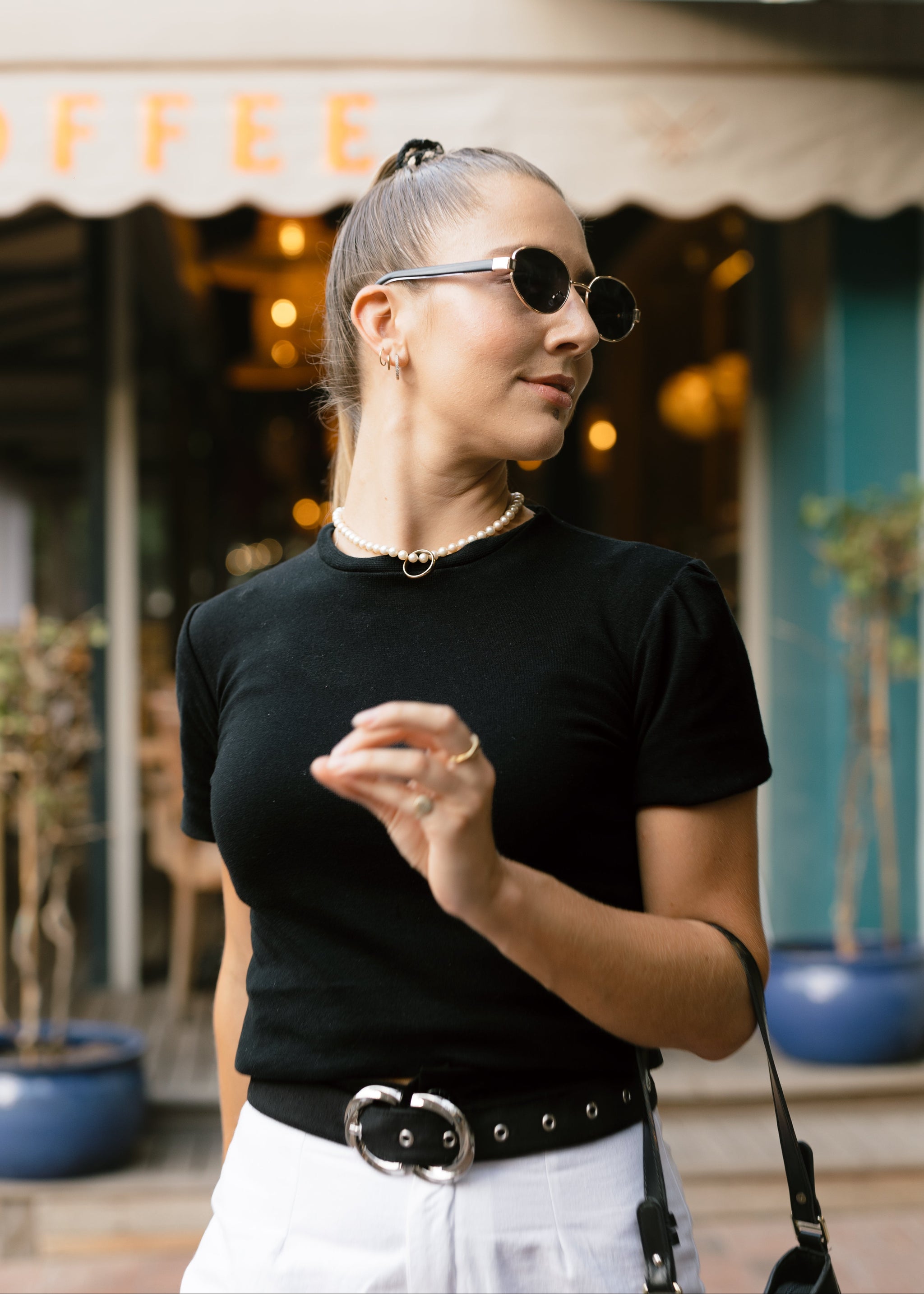 Woman wearing sunglasses and a black top in front of a coffee shop.