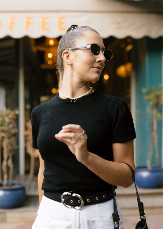Woman wearing sunglasses and a black top in front of a coffee shop.