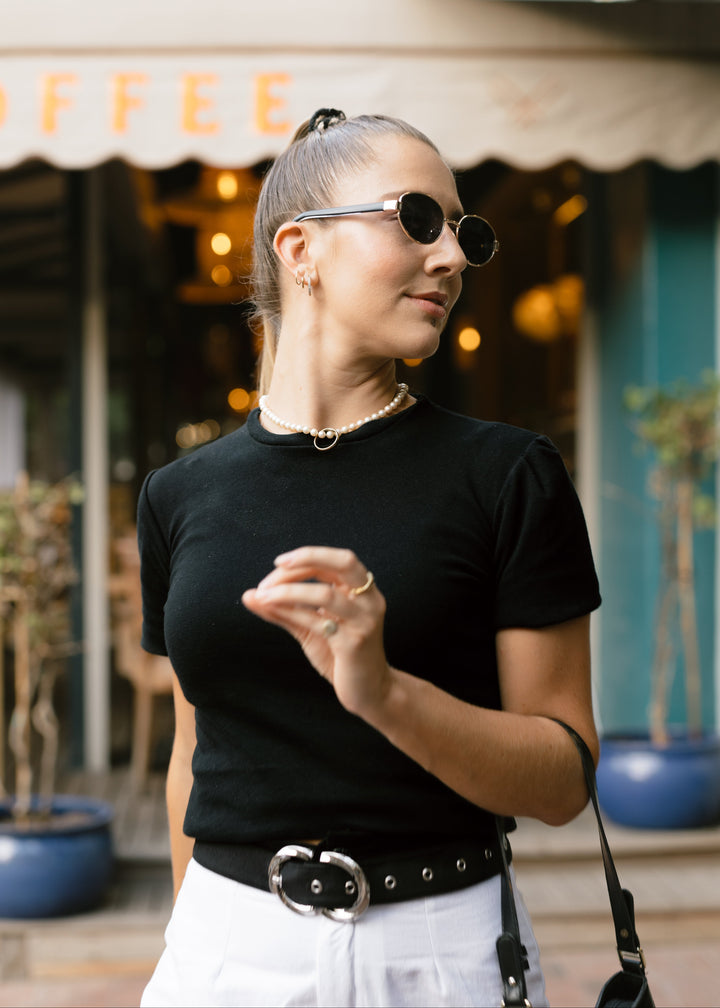 Woman wearing sunglasses and a black top in front of a coffee shop.