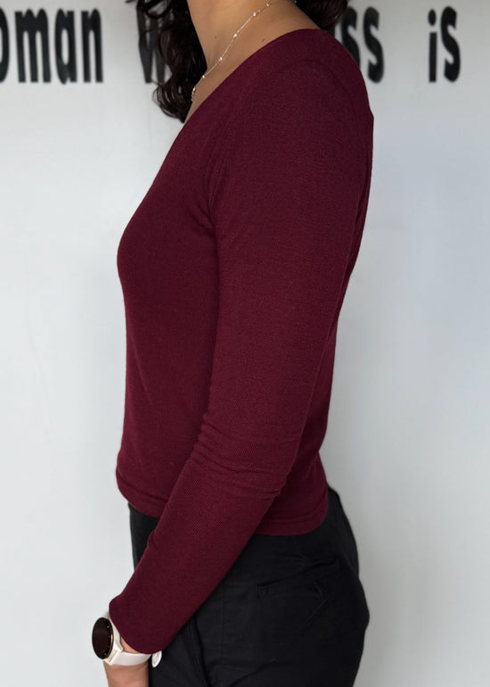 Person wearing a burgundy long-sleeve top against a white background with text.