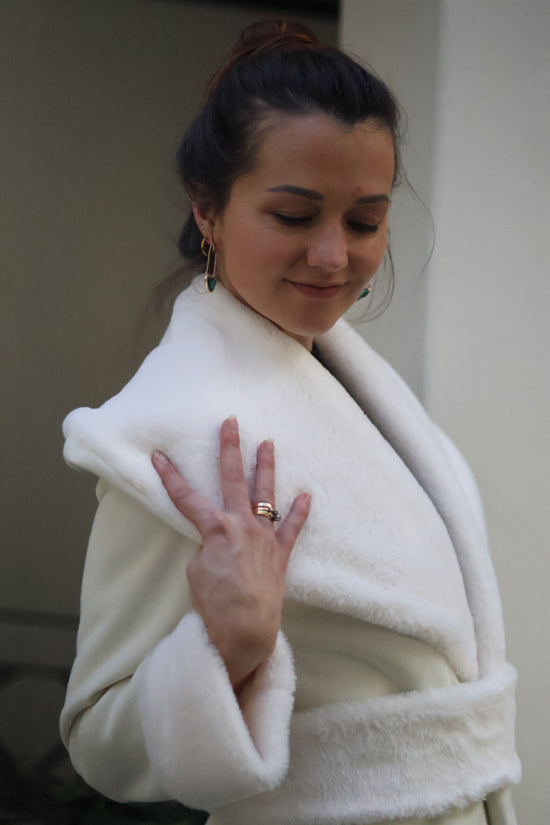 Woman wrapped in a white towel, possibly after a bath or shower, with a neutral background.
