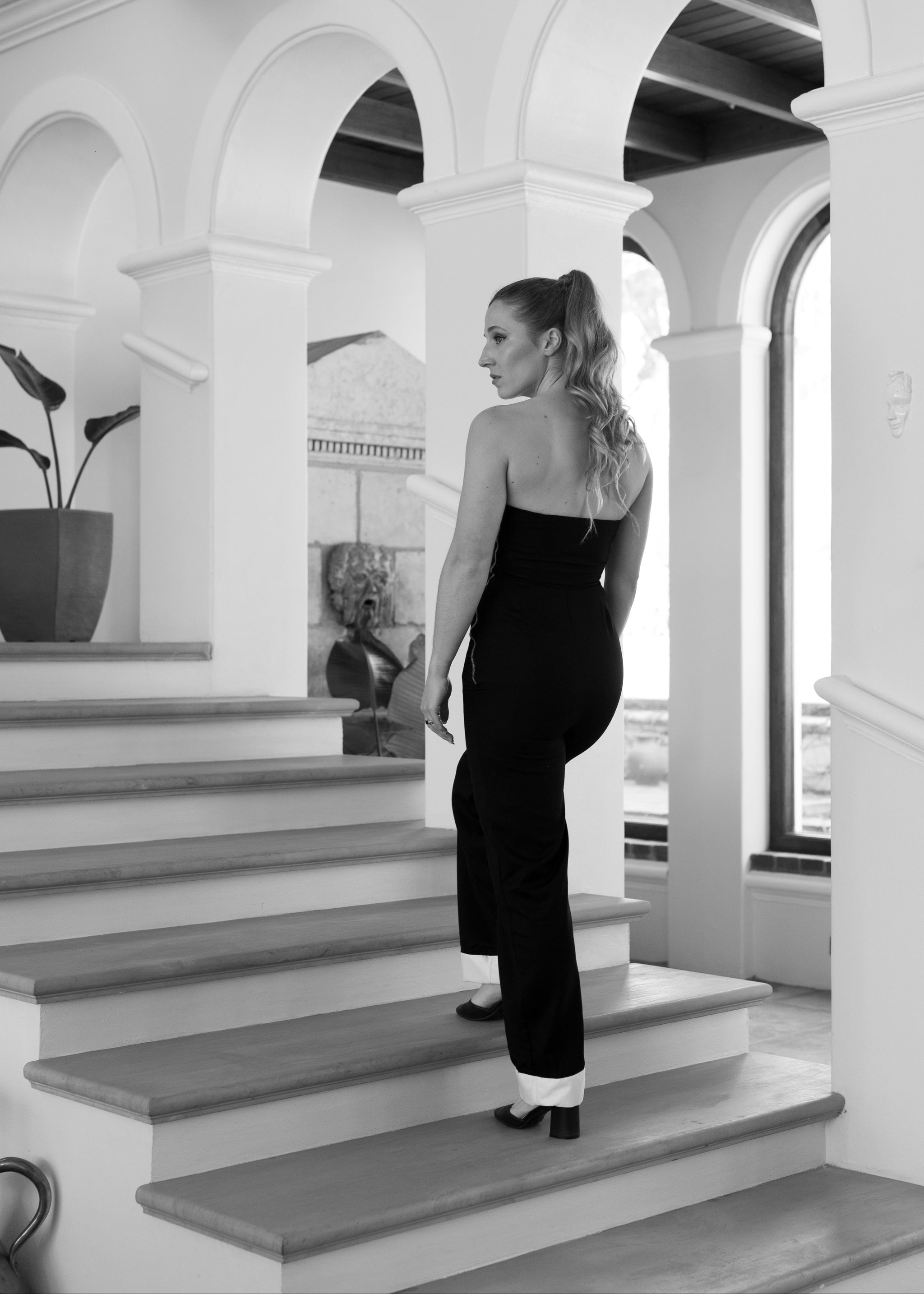 Woman in a black outfit standing on a staircase in an elegant interior setting