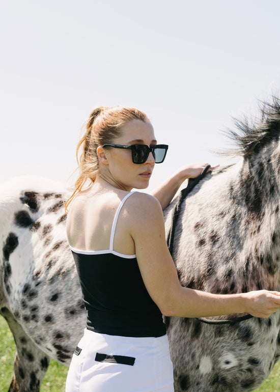Woman grooming a spotted horse in an outdoor setting