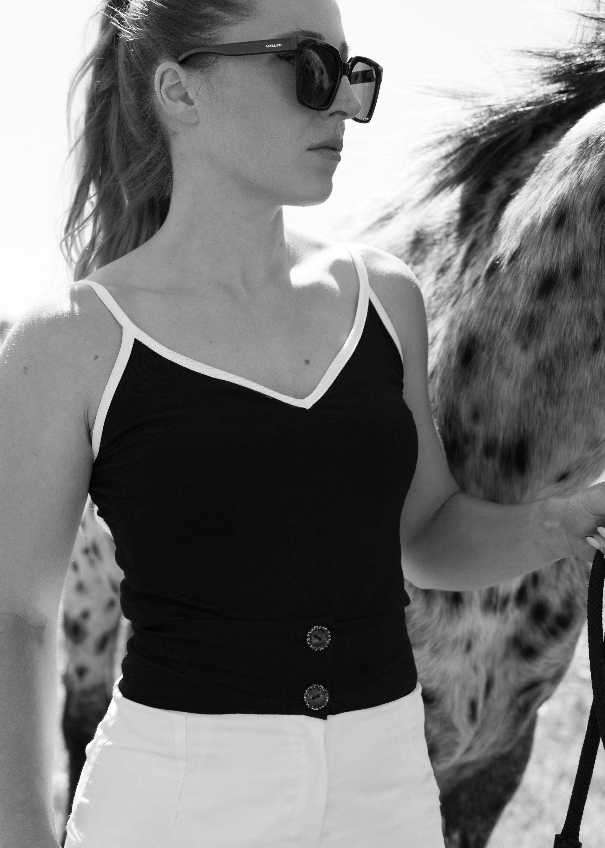 Woman wearing a black top and sunglasses standing next to a horse