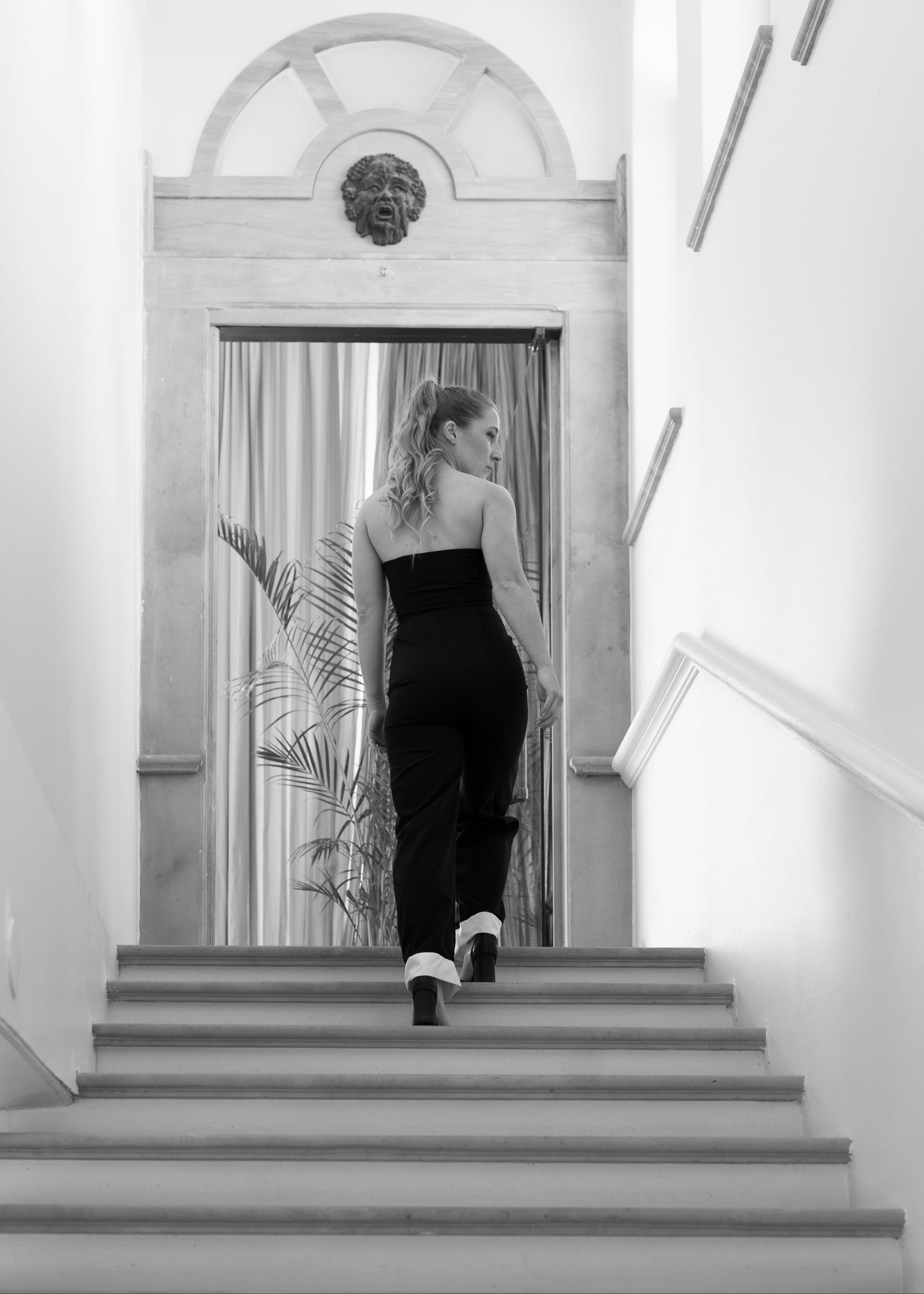 Woman in a black dress standing on a staircase with a decorative mirror behind her