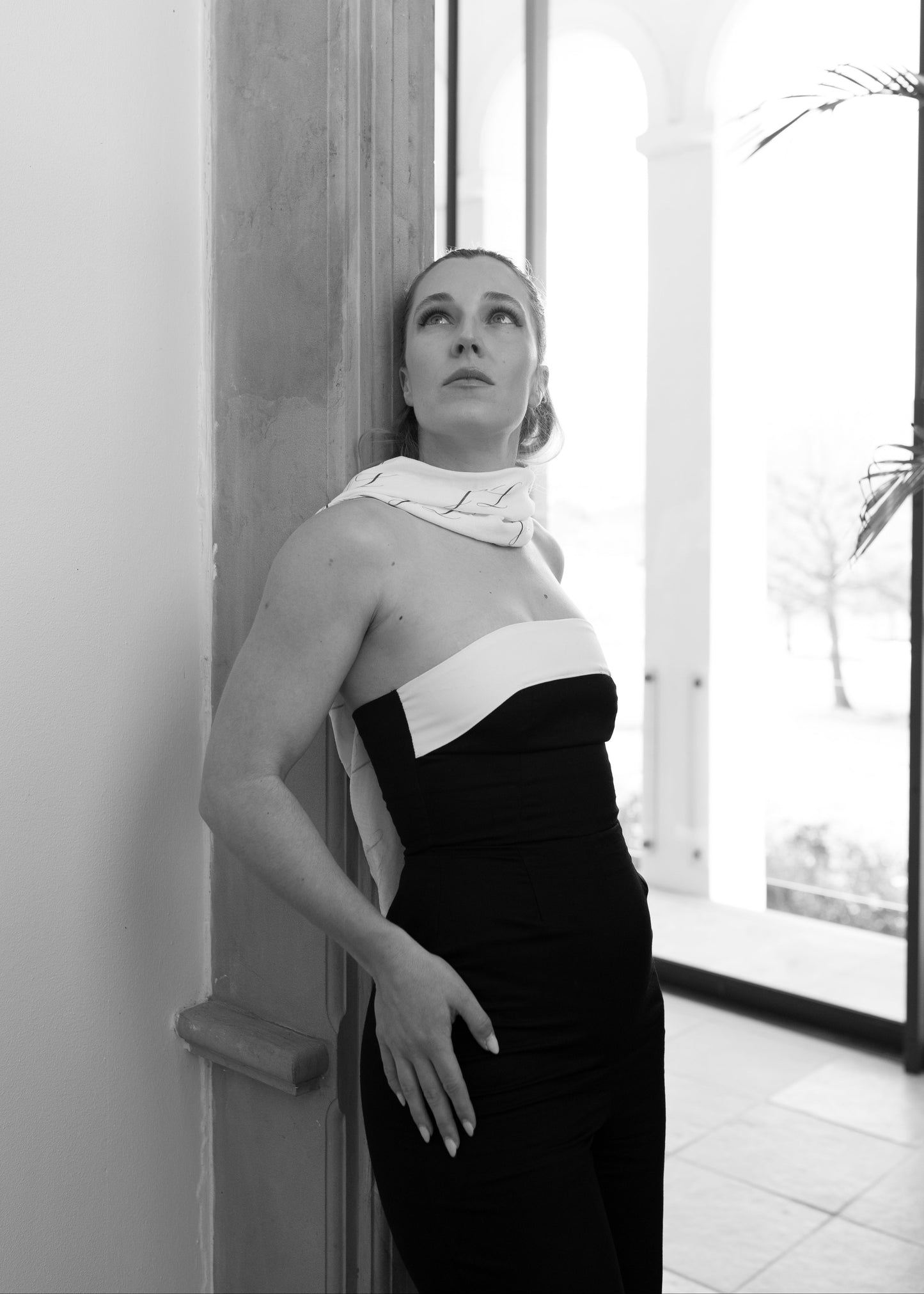 Black and white photo of a woman in a stylish dress leaning against a wall.