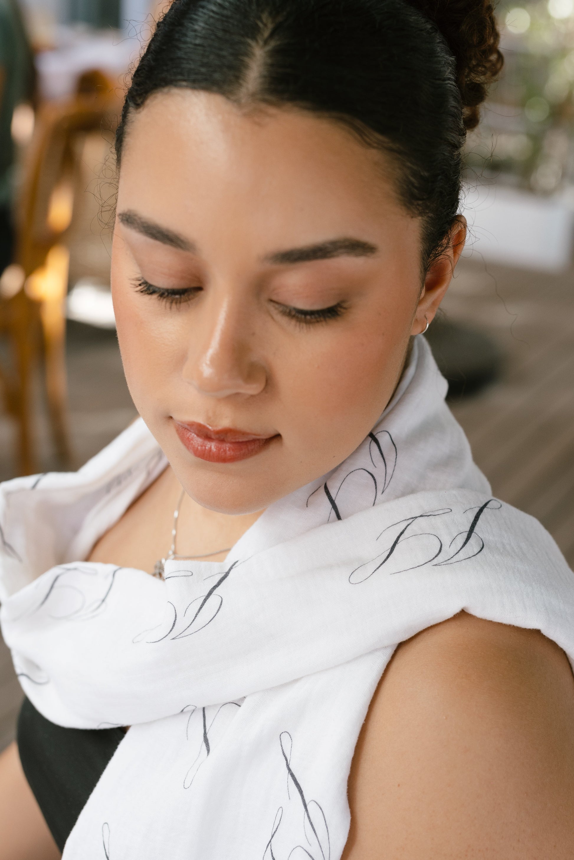 Woman wearing a white scarf with black patterns, looking down.