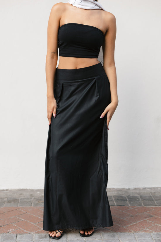 Woman wearing a black strapless top and long black skirt against a plain background