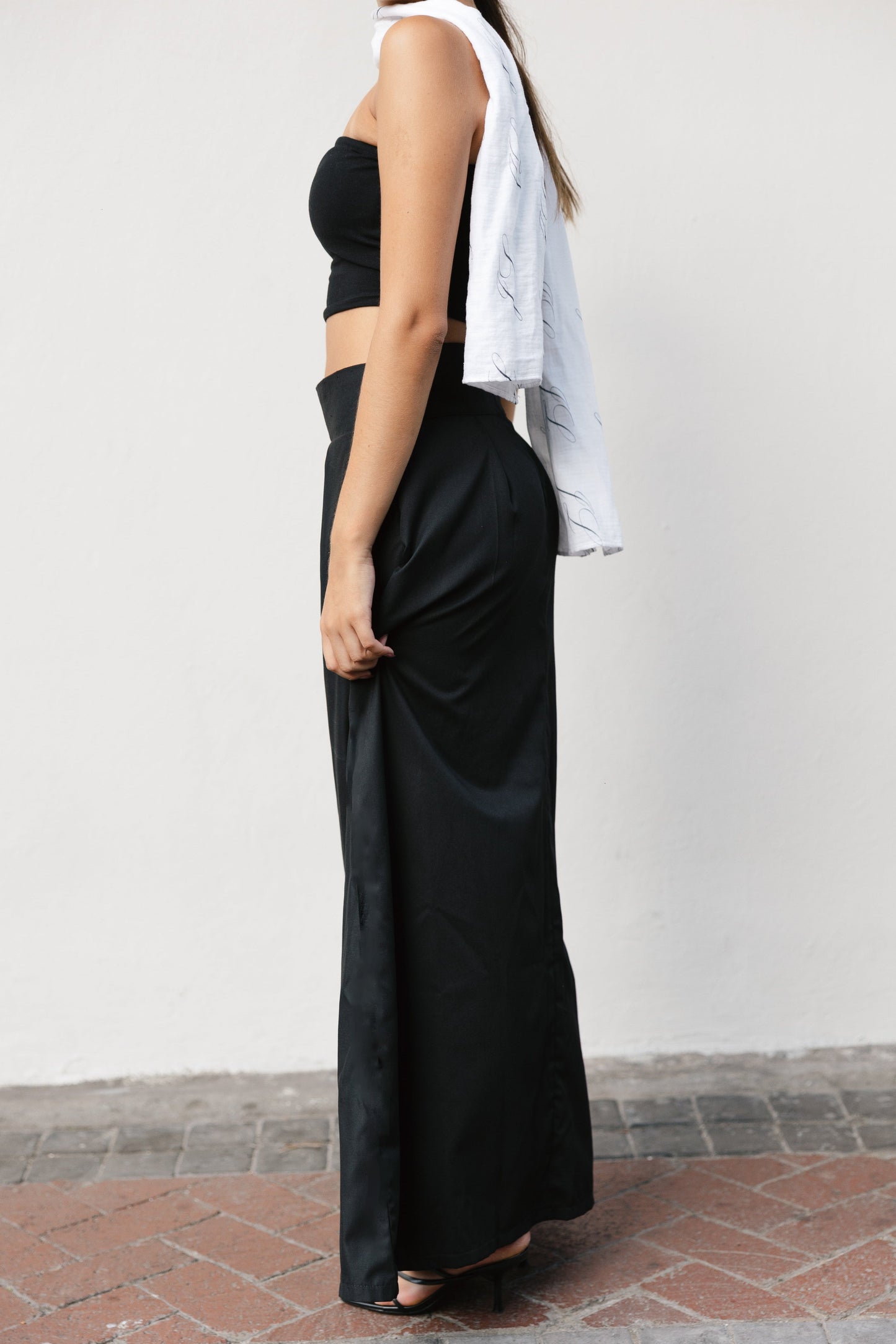 Person wearing a black outfit with a white shirt draped over one shoulder against a plain background