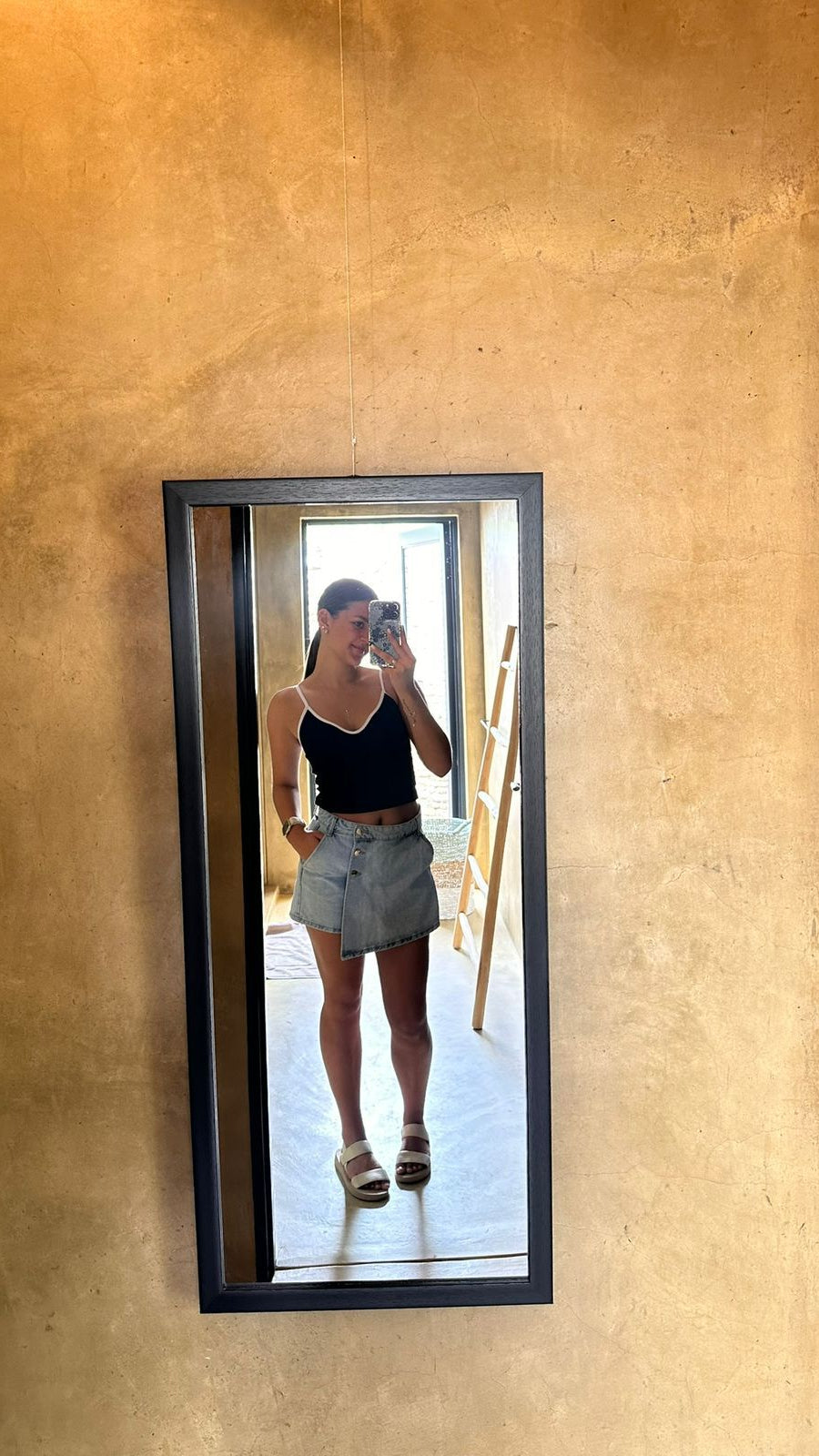Person taking a mirror selfie in a room with a textured beige wall.